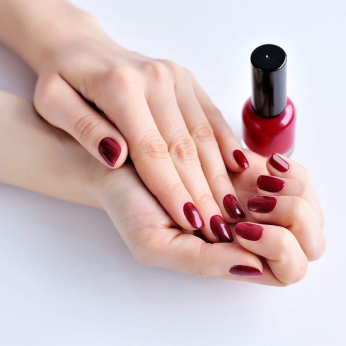 Hands of a woman with dark red manicure and nail polish bottle